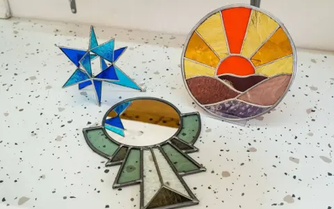 Trois pièces d'art en vitrail : une étoile bleue, un soleil couchant et un miroir ornemental. Créations d'un atelier vitrail Paris.