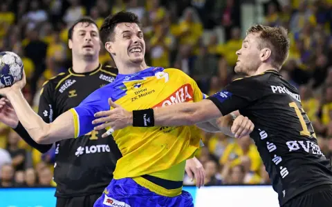 Zacięta walka na boisku. Zawodnik w żółtej koszulce z piłką ręczną, broni się przed przeciwnikiem. Emocje w meczu piłki ręcznej Kielce.