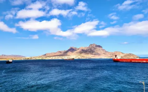 Blick auf die Bucht von Mindelo, Kap Verde, mit Schiffen im tiefblauen Wasser und einer bergigen Küstenlinie im Hintergrund.