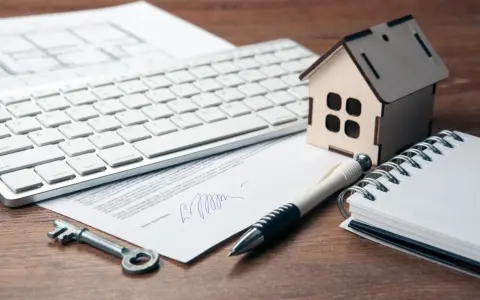 Clé, stylo, maison en bois, clavier et documents sur un bureau. Préparation de la résiliation assurance habitation.
