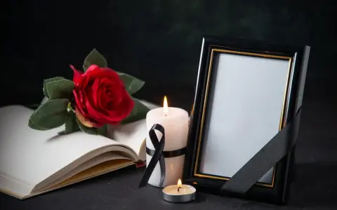 Pusta ramka na zdjęcie, płonące świece i czerwona róża na otwartej księdze. Symboliczne przedmioty wyrażające kondolencje.