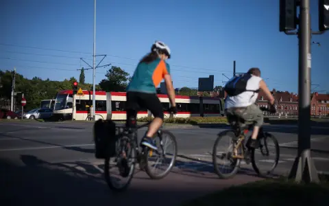 Rowerzyści jadący wzdłuż torów tramwajowych, w tle czerwono-biały tramwaj. Trasa rowerowa wiodąca w kierunku Westerplatte.