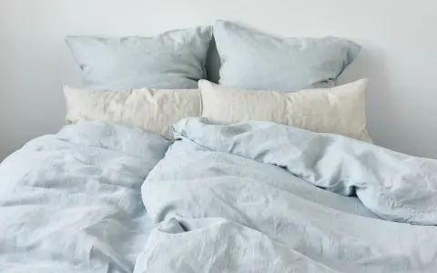 Ein Bett mit hellblauen und cremefarbenen Leinenbezügen. Perfekt für einen kühlen Sommerabend.
