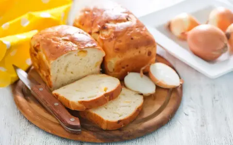 Zwiebelbrot rezept: goldbraune Brote mit Zwiebeln, angeschnitten, daneben Zwiebeln und ein Messer.