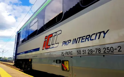 Pociąg PKP Intercity z napisem "Warszawa Poznań" na tle błękitnego nieba z chmurami.