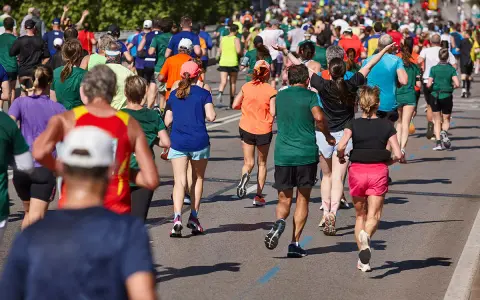 Tłum biegaczy pokonuje kolejne kilometry maratonu. Widać ich nogi w ruchu, kolorowe stroje i cienie na asfalcie.