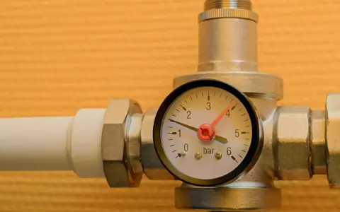 Un réducteur de pression d'eau avec un manomètre indiquant 1 bar. L'appareil est monté sur un tuyau blanc.