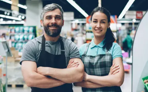 Deux employés souriants, habitués à rester debout toute la journée, posent dans un supermarché.