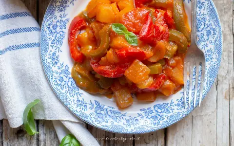Un piatto di peperonata con patate, colorata e saporita, guarnita con basilico fresco.