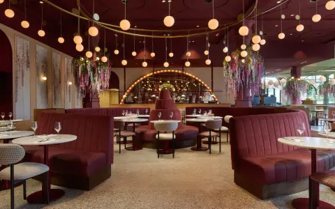 Efteling restaurant mit roten Samt-Sitzbänken, runden Marmortischen und üppigen Blumenarrangements. Hängende Kugelleuchten schaffen eine warme Atmosphäre.