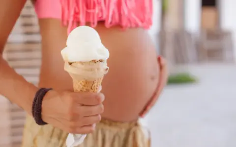 Schwanger und Lust auf Eis? Eine Frau hält eine Eistüte, während sie ihren Bauch streichelt.