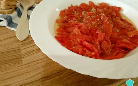 Asadillo manchego, pimientos asados con ajo y aceite, listos para disfrutar con tostadas y una cuchara de madera.