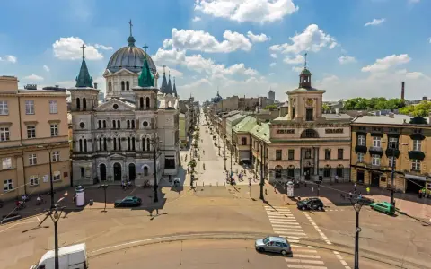 Widok na ulicę Piotrowską w Łodzi, z kościołem św. Stanisława Kostki i kamienicami. Tętniące życiem łódzkie stare miasto w słoneczny dzień.