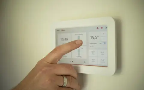 Dłoń dotyka ekranu, pokazując jak ustawić temperaturę w pompie ciepła. Widoczna aktualna temperatura 19,5°C.