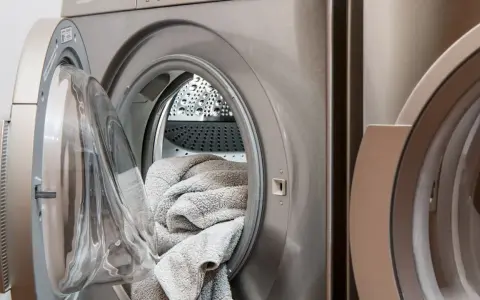 Eine offene Waschmaschine mit einem grauen Handtuch darin. Die Tür ist leicht geöffnet, um die Wäsche nach dem Waschen trocknen zu lassen.