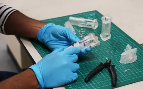 Hands in blue gloves assemble a 3D printed medical device prototype, showcasing innovation in healthcare technology.