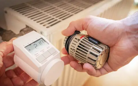Hände tauschen ein sehr altes Thermostat gegen ein modernes Gerät an einem Heizkörper.