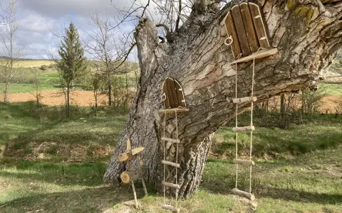Un árbol con dos pequeñas puertas de madera y escaleras de cuerda, invitando a un arbolón paseo mágico. Un ciervo de madera decora la base.