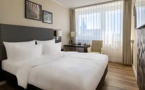 Przytulny pokój w hotelu Radisson Blu Erfurt z białym pościelonym łóżkiem, biurkiem i oknem z widokiem na miasto.