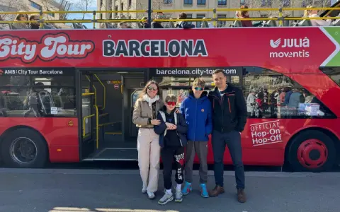 Family posing in front of a red "City Tour Barcelona" bus, ready for an adventure.
