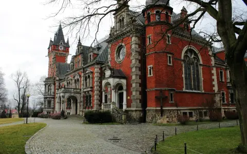 Pławniowice atrakcje: okazały pałac z czerwoną cegłą, wieżą zegarową i brukowanym dziedzińcem.