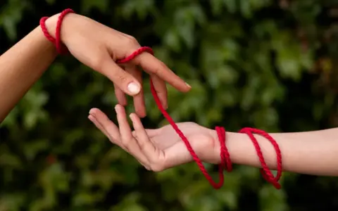 Dwie dłonie połączone czerwoną wstążką na ręce, symbolizującą więź.