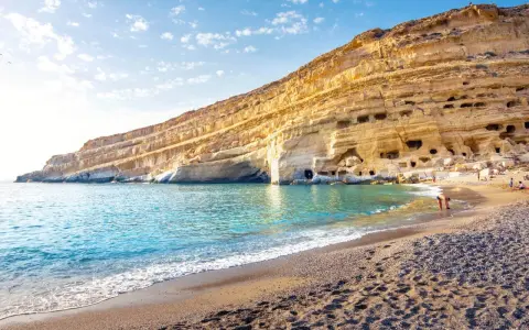 Ein malerischer Strand auf Kreta mit türkisfarbenem Wasser, das sanft an den Kiesstrand schwappt. Die beeindruckende Felswand mit ihren Höhlen bietet eine einzigartige Kulisse.