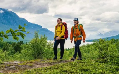 Två glada vandrare med ryggsäckar på en stig i fjällen. En perfekt plats att bo på efter en dag av vandring, kanske på ett STF vandrarhem.