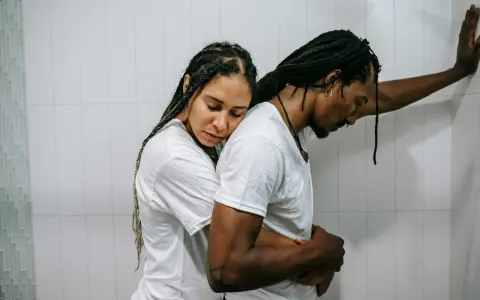 Una pareja se abraza con tristeza, reflejando el momento en que empiezan los problemas de pareja. Él se apoya en la pared, ella recuesta su cabeza en su hombro.