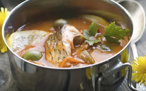 Aromaticzna rosyjska zupa rybna w metalowej misce, z kawałkami ryby, oliwkami, cytryną i natką pietruszki.