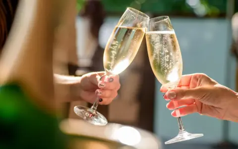 Zwei Hände stoßen mit Gläsern an, gefüllt mit prickelndem alkoholfreiem Sekt. Perfekt für die Schwangerschaft und besondere Anlässe.