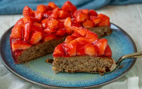 Ein saftiger, glutenfreier Erdbeerkuchen mit frischen Erdbeeren und glänzender Tortenglasur auf einem blauen Teller.