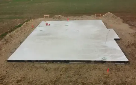 Płyta fundamentowa koszt. Betonowa płyta na budowie, otoczona ziemią i elementami instalacji.