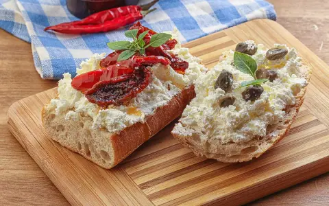 Dwa kawałki bagietki z twarogiem, suszonymi pomidorami i kaparami. Kapary dodają wyrazistego smaku, świetnie komponując się z serem i pomidorami.