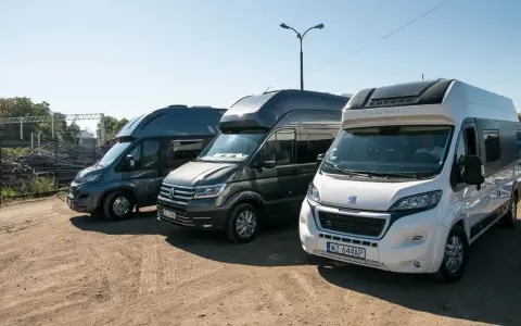 Trzy kampery stoją obok siebie na placu. Jeden z nich to kamper VW w ciemnoszarym kolorze.