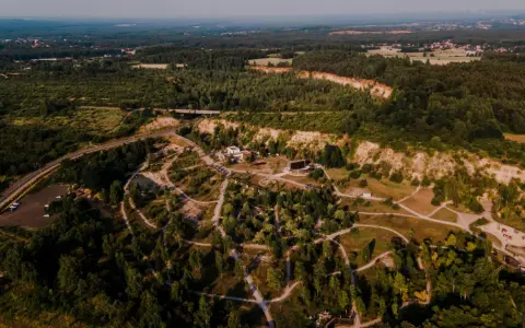 Widok z lotu ptaka na krajobraz z lasami, drogą i budynkami. W oddali widać miasto. To miejsce przypomina ptasią rzeczpospolitą, gdzie natura i cywilizacja współistnieją.