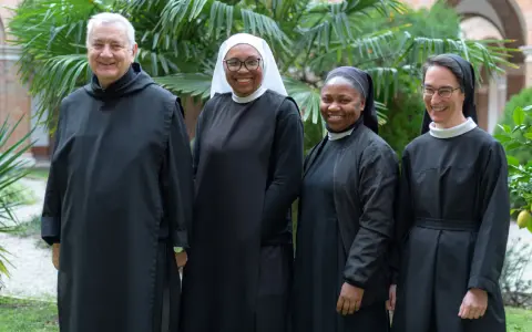 Four individuals in Benedictine habit smile in a garden.