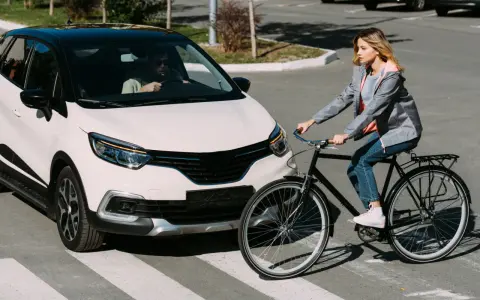Frau auf Fahrrad kreuzt Straße, Auto hält an. Die Szene erinnert an die **Bremsweg Formel** für Verkehrssicherheit.