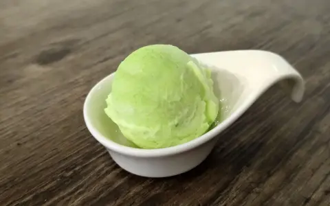 Una bola de helado de manzana verde brillante en una taza blanca sobre una mesa de madera.