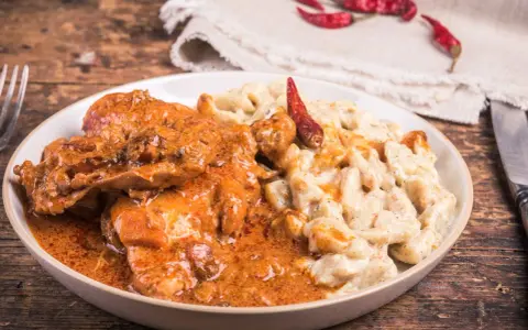 Gulasz z warzywami, podany z kremowym sosem i ozdobiony suszonymi papryczkami chili, kusi apetycznym wyglądem.
