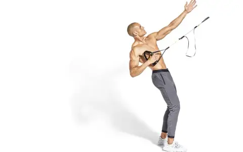 Hombre musculoso realiza ejercicio de remo TRX, con su brazo extendido hacia arriba y el otro sujetando las asas.