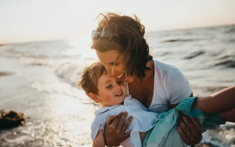 Ciepły moment na plaży, kiedy dziecko daje buziaka mamie. Słońce odbija się w falach.