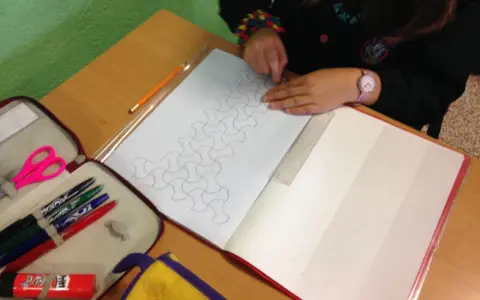 Bambina disegna un motivo geometrico su un quaderno di matematica. Matite, forbici e righello a portata di mano.