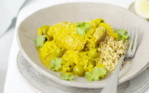 Un plat de tajine poulet citron, parfumé et coloré, servi avec du couscous et des olives vertes.