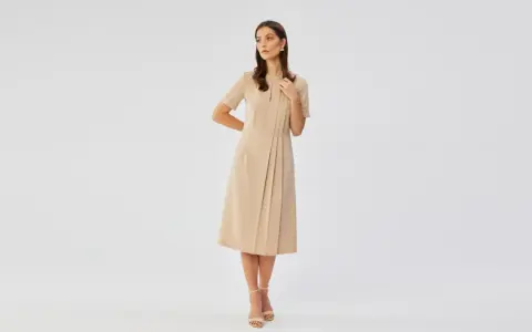 Elegancka beżowa sukienka to idealna propozycja, jak się ubrać na wesele po 50. Klasyczna, ale stylowa.