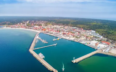 Widok z lotu ptaka na malowniczy hel port z licznymi łodziami i statkami. W tle rozciąga się miasto i las.
