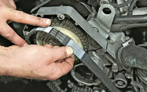 Hände montieren einen neuen Zahnriemen an einem Motor. So gelingt der Zahnriemenwechsel selbst.