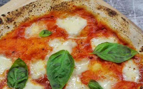 Ein Stück italienische Pizza Margherita mit geschmolzenem Mozzarella, Tomatensauce und frischem Basilikum. Perfekt für ein authentisches italien pizza rezept.