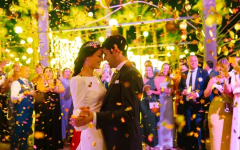 Novios bailando bajo confeti dorado. Invitados sonríen y celebran. ¡Ideas para bodas divertidas!