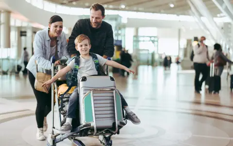 Familj på flygplatsen med ett barn sittandes på handbagage. De är glada och redo för sin resa.